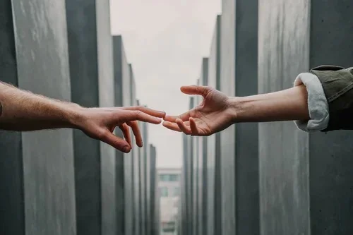 Two people reaching across a gap to touch fingertips